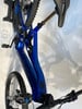 Ein blaues Mountain-E-Bike hängt an der Wand, mit sichtbarer Federung und Pedal.