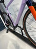 Ein lila Fahrradrahmen mit orangefarbenen und dunkelblauen Details wird gezeigt.