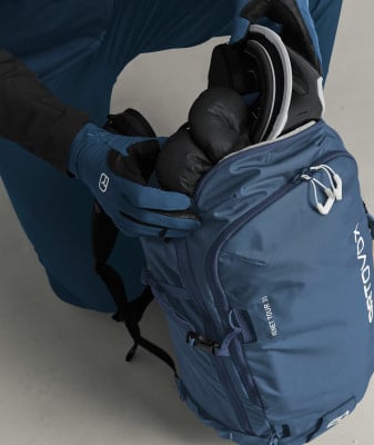 Ein Mann packt eine Skibrille und Handschuhe in einen Rucksack. Ein Mann packt eine Skibrille und Handschuhe in einen Rucksack.