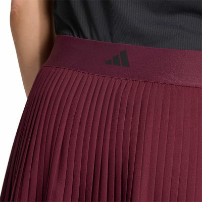 Detail eines plissierten roten Rocks mit Adidas-Logo auf einem dunkelroten Bund. Detail eines plissierten roten Rocks mit Adidas-Logo auf einem dunkelroten Bund.