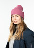 Eine Frau mit einer rosa Mütze und einer dunkelblauen Jacke posiert vor einem weißen Hintergrund.