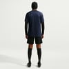 Ein Mann von hinten in einem dunkelblauen T-Shirt, schwarzer Hose und Socken.