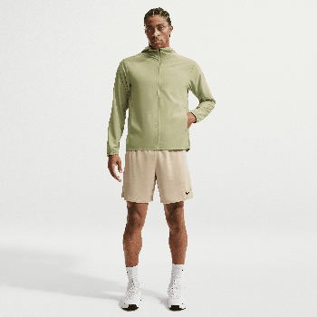 Mann in grüner Kapuzenjacke und beiger Shorts steht.