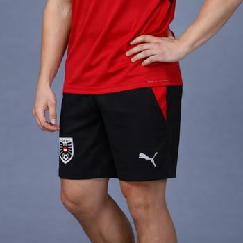 Ein Mann trägt ein rotes T-Shirt und eine schwarze Shorts mit PUMA-Logo und österreichischem Wappen.