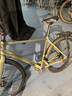 Ein grünes Cube-Fahrrad mit Gepäckträger und Schutzblechen steht auf einem blauen Teppich.