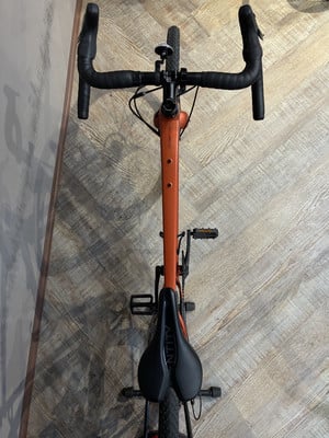Orangefarbenes Fahrrad mit schwarzem Lenker und Sattel auf Holzboden. Orangefarbenes Fahrrad mit schwarzem Lenker und Sattel auf Holzboden.