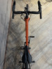 Orangefarbenes Fahrrad mit schwarzem Lenker und Sattel auf Holzboden.