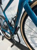 Blauer Gravelbike mit braunen Details und schwarzen Pedalen auf einem Ständer.