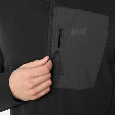 Detail einer schwarzen Jacke mit HH-Logo und Reißverschlusstasche, die von einer Hand gehalten wird. Detail einer schwarzen Jacke mit HH-Logo und Reißverschlusstasche, die von einer Hand gehalten wird.