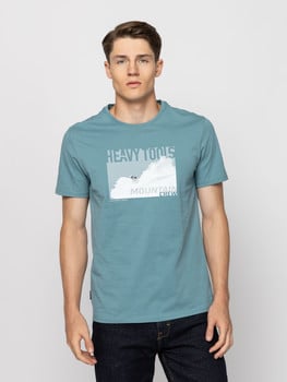 Egy férfi kék pólóban, hegyi mintával és a Mountain Crew felirattal.