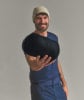 Ein Mann mit einer beige Mütze und blauem T-Shirt hält einen gefalteten schwarzen Schlafsack.