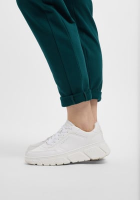 Weiße Damen-Sneaker zu dunkelgrünen Hosen mit hochgekrempelten Säumen. Weiße Damen-Sneaker zu dunkelgrünen Hosen mit hochgekrempelten Säumen.
