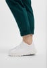 Weiße Damen-Sneaker zu dunkelgrünen Hosen mit hochgekrempelten Säumen.