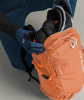 Skifahrer packt Handschuhe und Helm in einen orangefarbenen Rucksack.