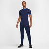 Ein Mann in einem dunkelblauen Nike-T-Shirt und Trainingshose steht vor weißem Hintergrund.