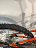 Das Hinterrad eines Mountainbikes mit orangefarbenem Rahmen und Dämpfung.