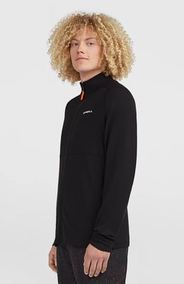 Ein Mann mit lockigem Haar trägt eine schwarze Jacke mit orangefarbenem Reißverschluss.