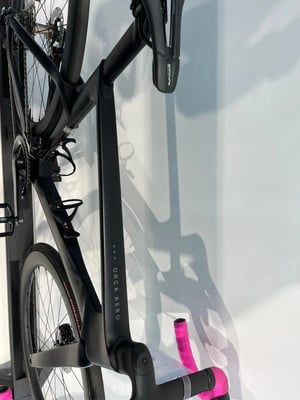 Ein schwarzes Rennrad mit pinkem Lenkerband hängt an der Wand.