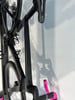 Ein schwarzes Rennrad mit pinkem Lenkerband hängt an der Wand.