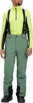 Ein Mann in grüner Skihose und gelbem Stehkragenpullover mit schwarzen Akzenten.