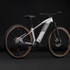 Graues E-Bike mit schwarzem Sattel und braunen Reifen auf schwarzem Hintergrund.