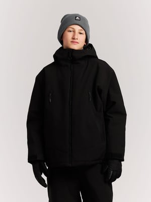 Ein Junge in schwarzer Winterjacke und grauer Mütze steht vor weißem Hintergrund.