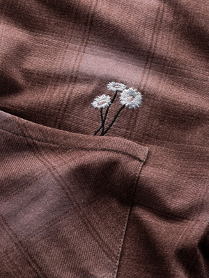 Brauner karierter Stoff mit gestickten Gänseblümchen auf der Tasche. Brauner karierter Stoff mit gestickten Gänseblümchen auf der Tasche.
