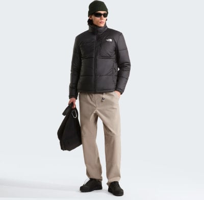 Ein Mann in einer schwarzen Daunenjacke und beigen Hosen hält eine Tasche. Ein Mann in einer schwarzen Daunenjacke und beigen Hosen hält eine Tasche.