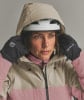 Eine Frau passt die Kapuze einer Skijacke mit Helm und Handschuhen an.