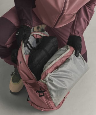 Eine Person packt schwarze Kleidung und Handschuhe in einen rosa Rucksack.