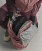 Eine Person packt schwarze Kleidung und Handschuhe in einen rosa Rucksack.