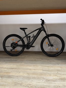 Schwarzes Mountain-E-Bike mit Federung und Scheibenbremsen auf Holzboden.