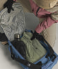 Eine Person packt eine Jacke und Handschuhe in eine blaue Tasche mit vielen Fächern.