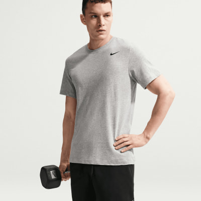 Ein Mann im grauen Nike-T-Shirt hält eine Hantel und hat eine Hand in der Hüfte.
