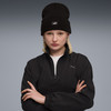 Eine Frau in einer schwarzen Mütze und Jacke mit Puma-Logo, die Arme vor der Brust verschränkt.
