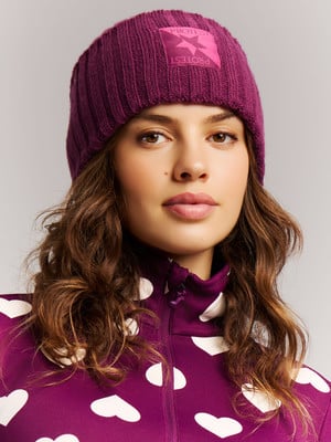 Ein Mädchen trägt eine lila Mütze mit Logo und eine lila Jacke mit Herzen.