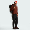Ein Mann in einer braunen Jacke und schwarzer Hose mit Rucksack.