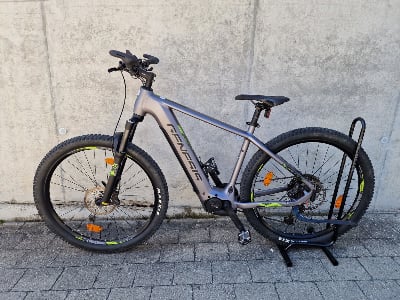Ein graues Genesis E-Bike mit Federung und breiten Reifen steht auf einem Pflasterstein. Ein graues Genesis E-Bike mit Federung und breiten Reifen steht auf einem Pflasterstein.