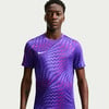 Ein Mann in einem lila T-Shirt mit geometrischem Muster und Nike-Logo.