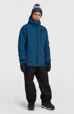 Ein junger Mann in einer blauen Winterjacke, schwarzer Hose und Bommelmütze.