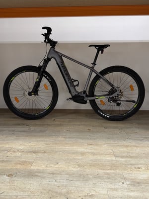 Ein graues E-Mountainbike mit schwarzen Rädern steht auf einem Holzboden. Ein graues E-Mountainbike mit schwarzen Rädern steht auf einem Holzboden.