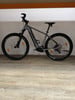 Ein graues E-Mountainbike mit schwarzen Rädern steht auf einem Holzboden.