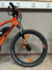 Ein orangefarbenes E-Mountainbike mit schwarzen Details und Federung vorne.