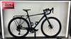 Ein grünes Fahrrad mit Gepäckträger und Firmenlogo auf rotem Schild.