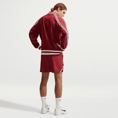 Ein Mann in einer roten Jacke und Shorts steht seitlich zur Kamera. Ein Mann in einer roten Jacke und Shorts steht seitlich zur Kamera.