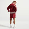 Ein Mann in einer roten Jacke und Shorts steht seitlich zur Kamera.
