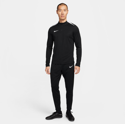 Ein Mann in einem schwarzen Nike-Trainingsanzug steht vor einem weißen Hintergrund.