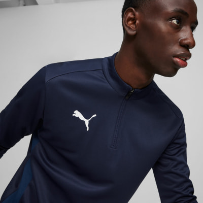 Ein Mann in einer dunkelblauen Jacke mit Puma-Logo und kurzem Reißverschluss. Ein Mann in einer dunkelblauen Jacke mit Puma-Logo und kurzem Reißverschluss.