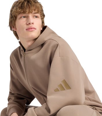 Junger Mann im braunen Hoodie mit Adidas-Logo auf dem Ärmel. Junger Mann im braunen Hoodie mit Adidas-Logo auf dem Ärmel.