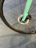 Detail des Vorderrads und der Bremse an einem teal-farbenen Fahrrad.